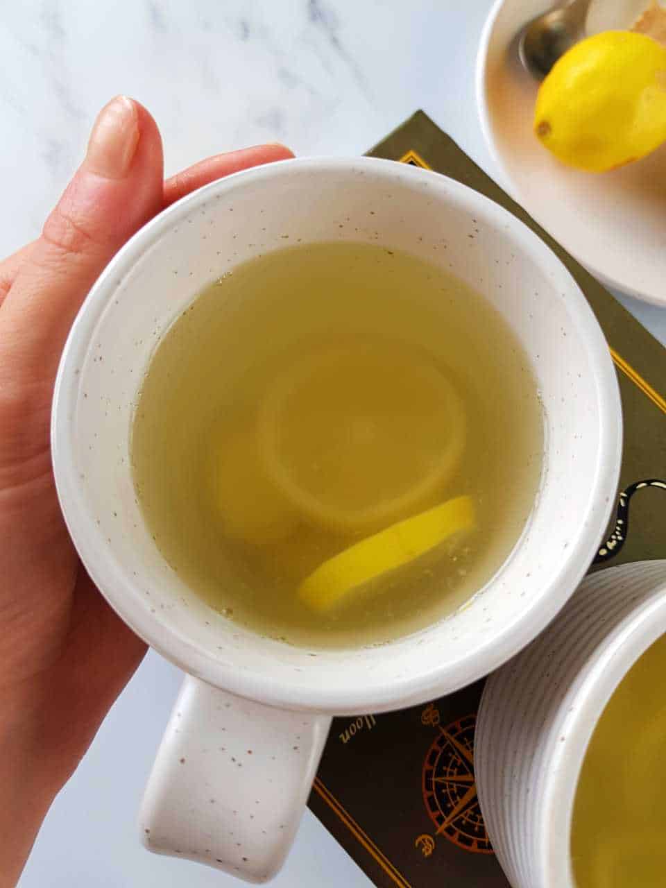 Lemon and ginger tea in a white cup comforted by a hand.