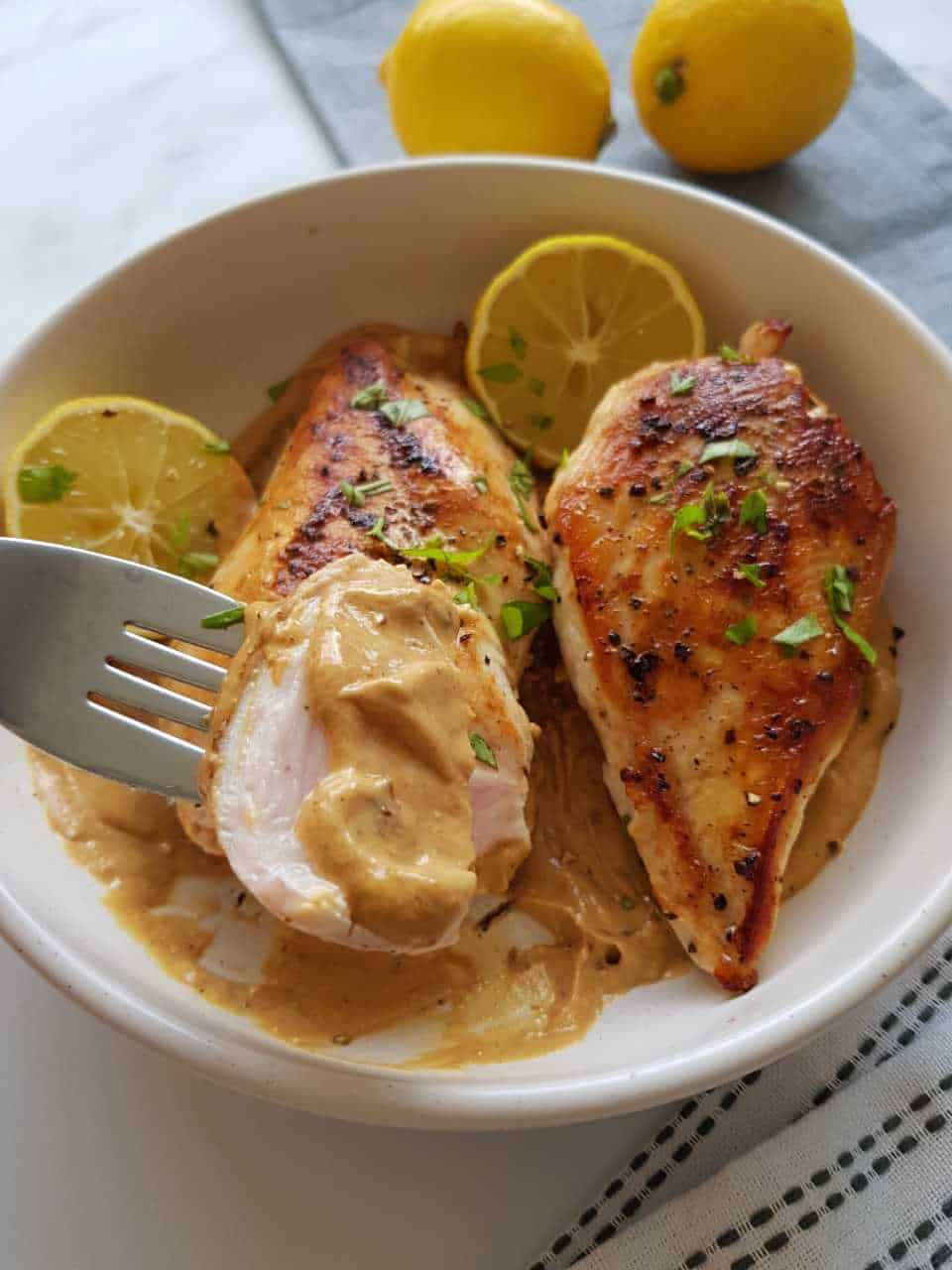 Lemon pepper chicken breasts in a white bowl with lemons in the background.