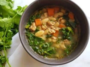 Mediterranean soup with sausage and beans in a grey bowl on a marble table.