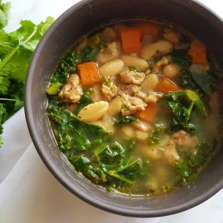 Mediterranean soup with sausage and beans in a grey bowl on a marble table.