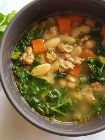 Mediterranean soup with sausage and beans in a grey bowl on a marble table.