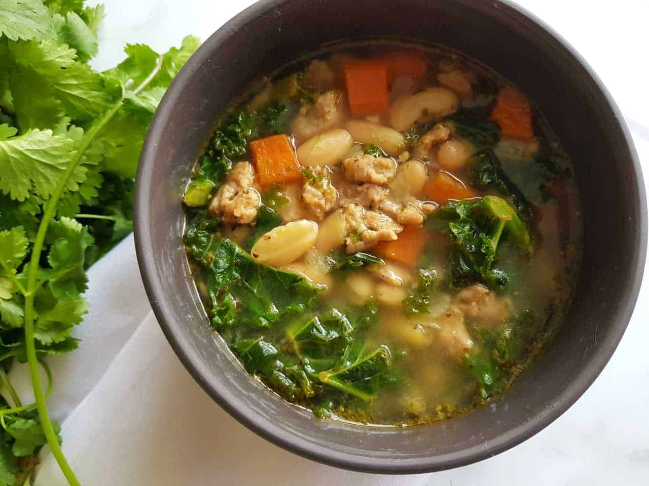 Mediterranean soup with sausage and beans in a grey bowl on a marble table.