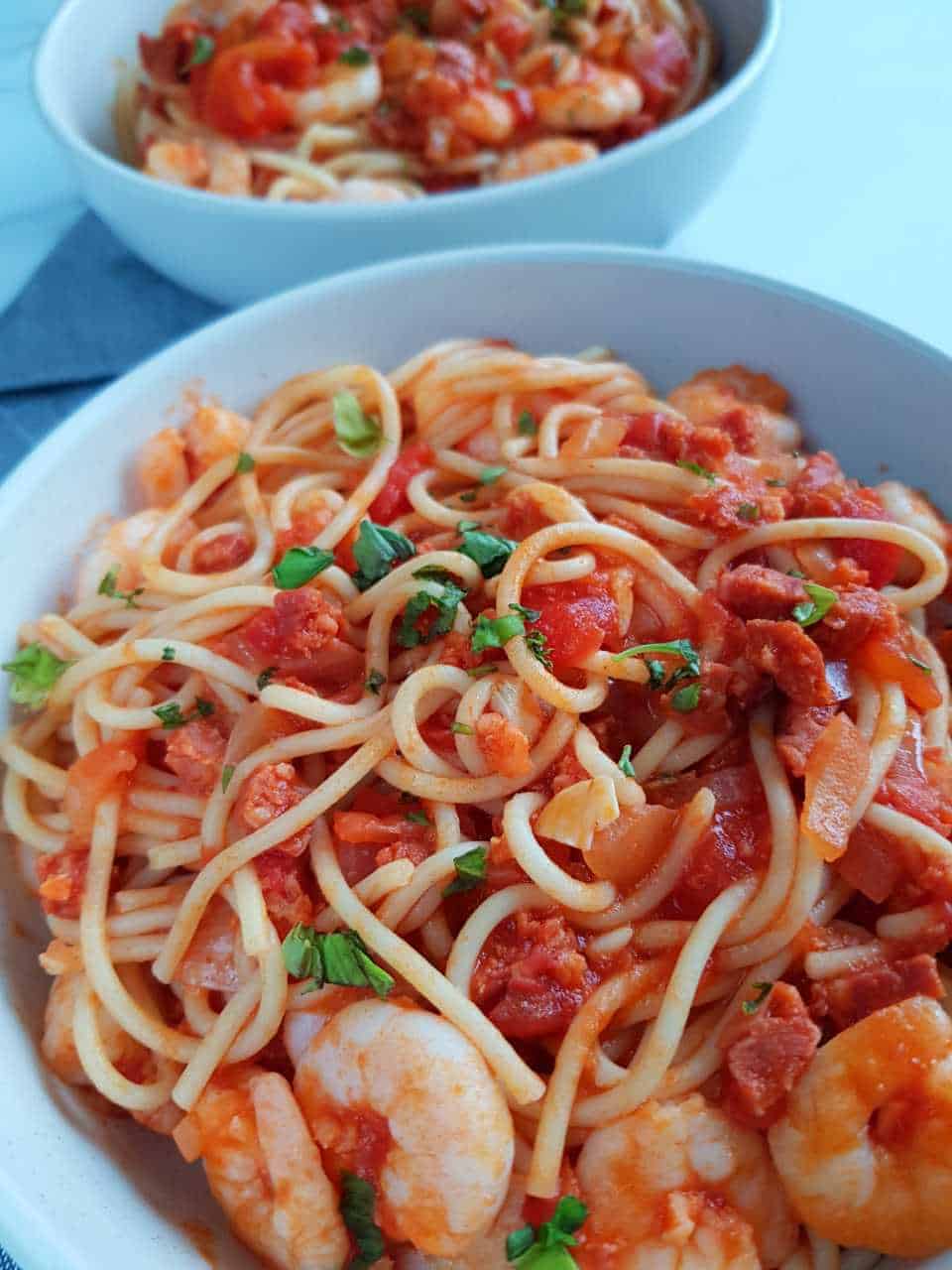 Pasta with prawns and chorizo in white bowls.