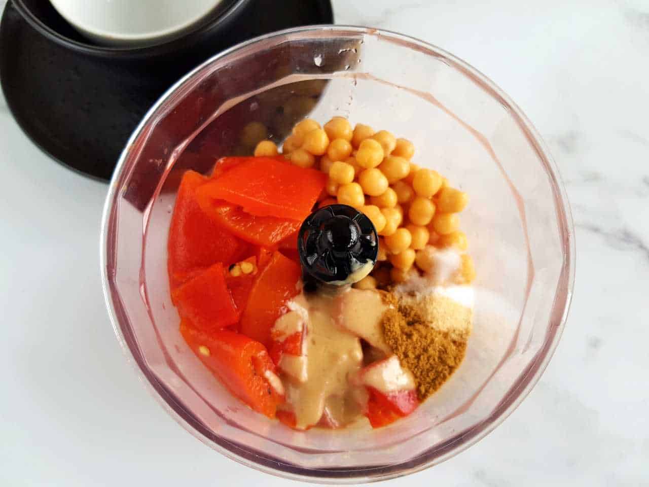 Peppers and chickpeas in a food processor on a marble table.