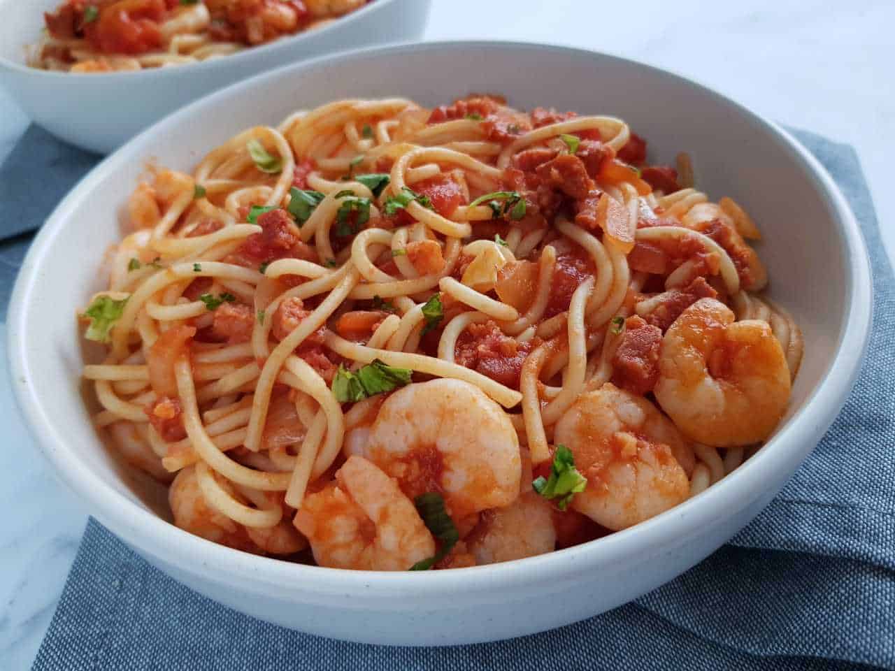 Prawn and chorizo pasta in a white bowl on a gray table cloth.