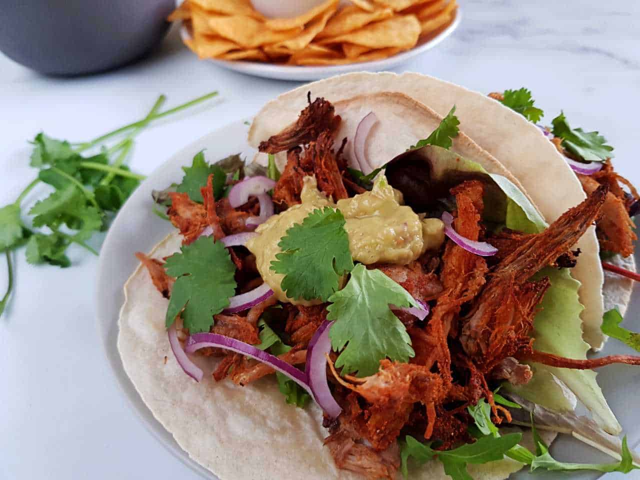 Pulled pork carnitas on a marble table with nachos inthe background.