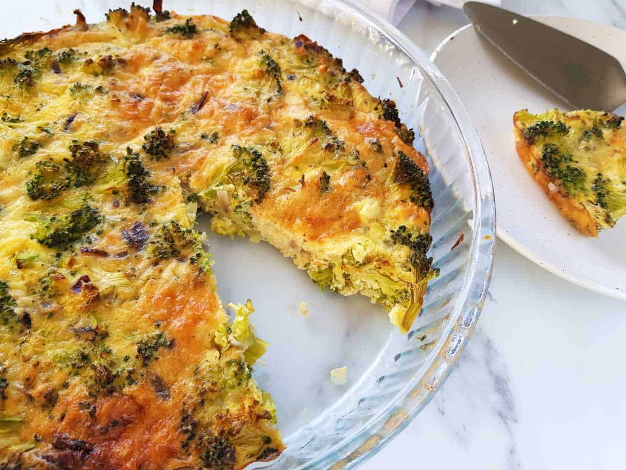 Quiche without crust in a quiche tin. A slice served on a white plate next to it.