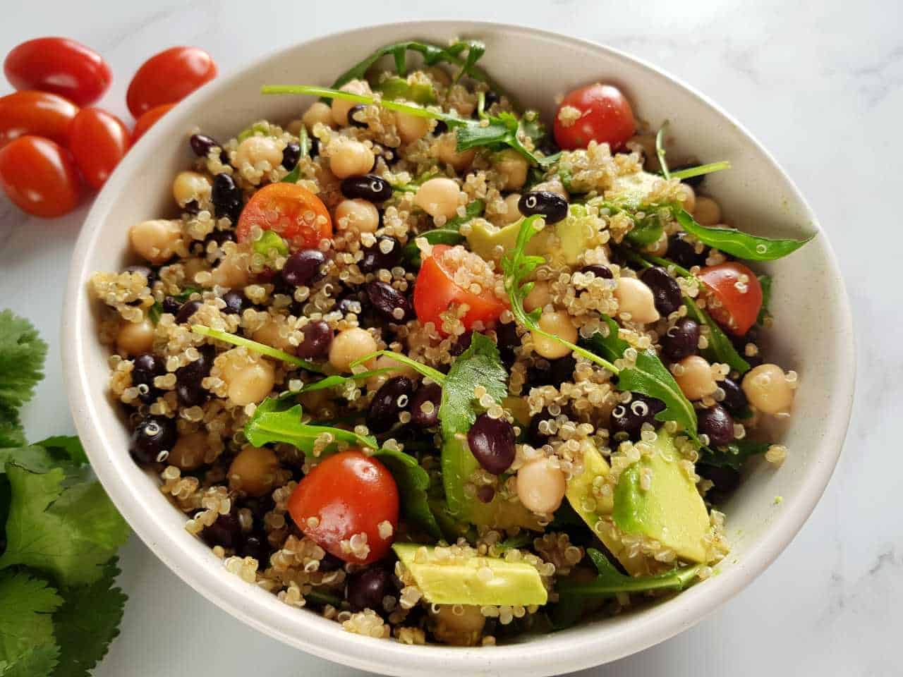 Quinoa black bean salad in a white bowl with tomatoes in the background.