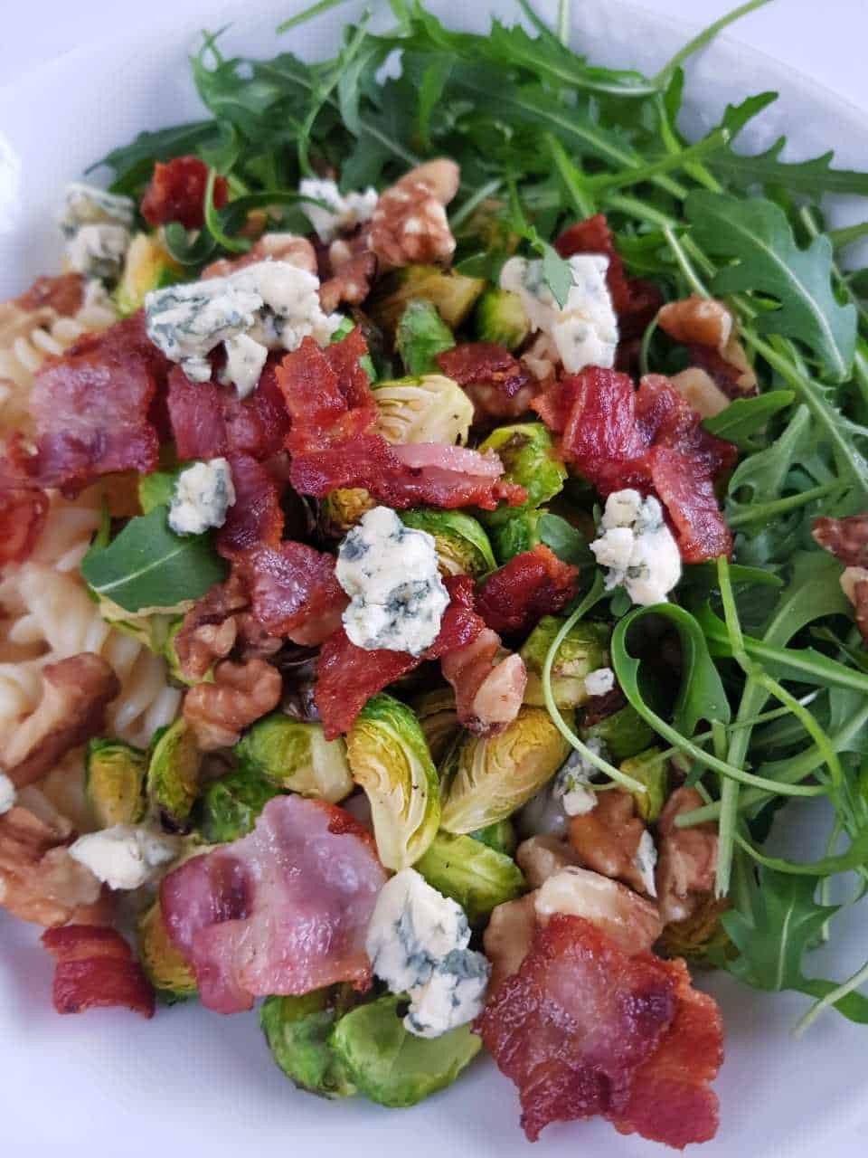 Salad with bacon, brussels sprouts and blue cheese in a white bowl.