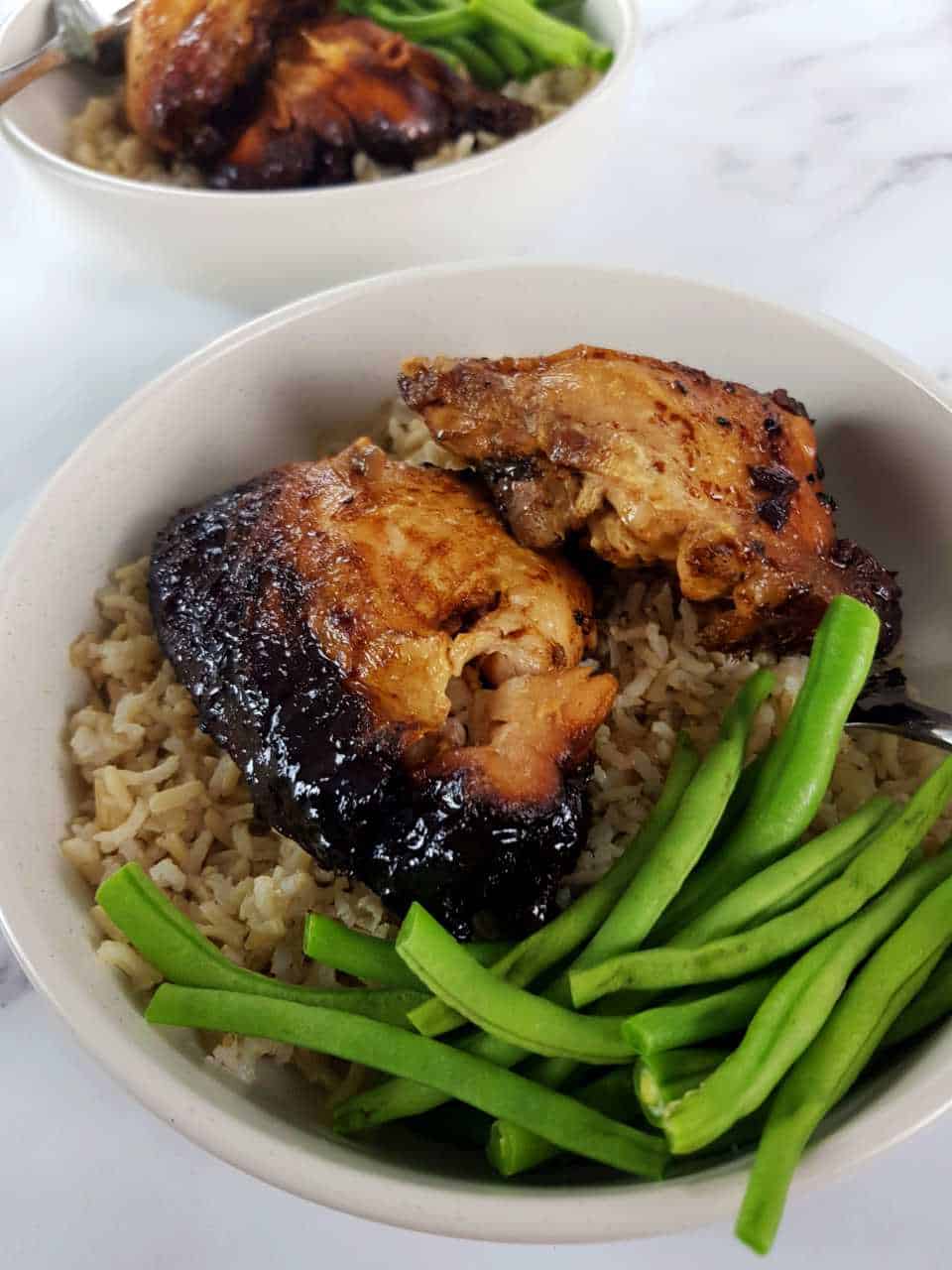 Slow cooker chicken adobo in white bowls on a marble table.