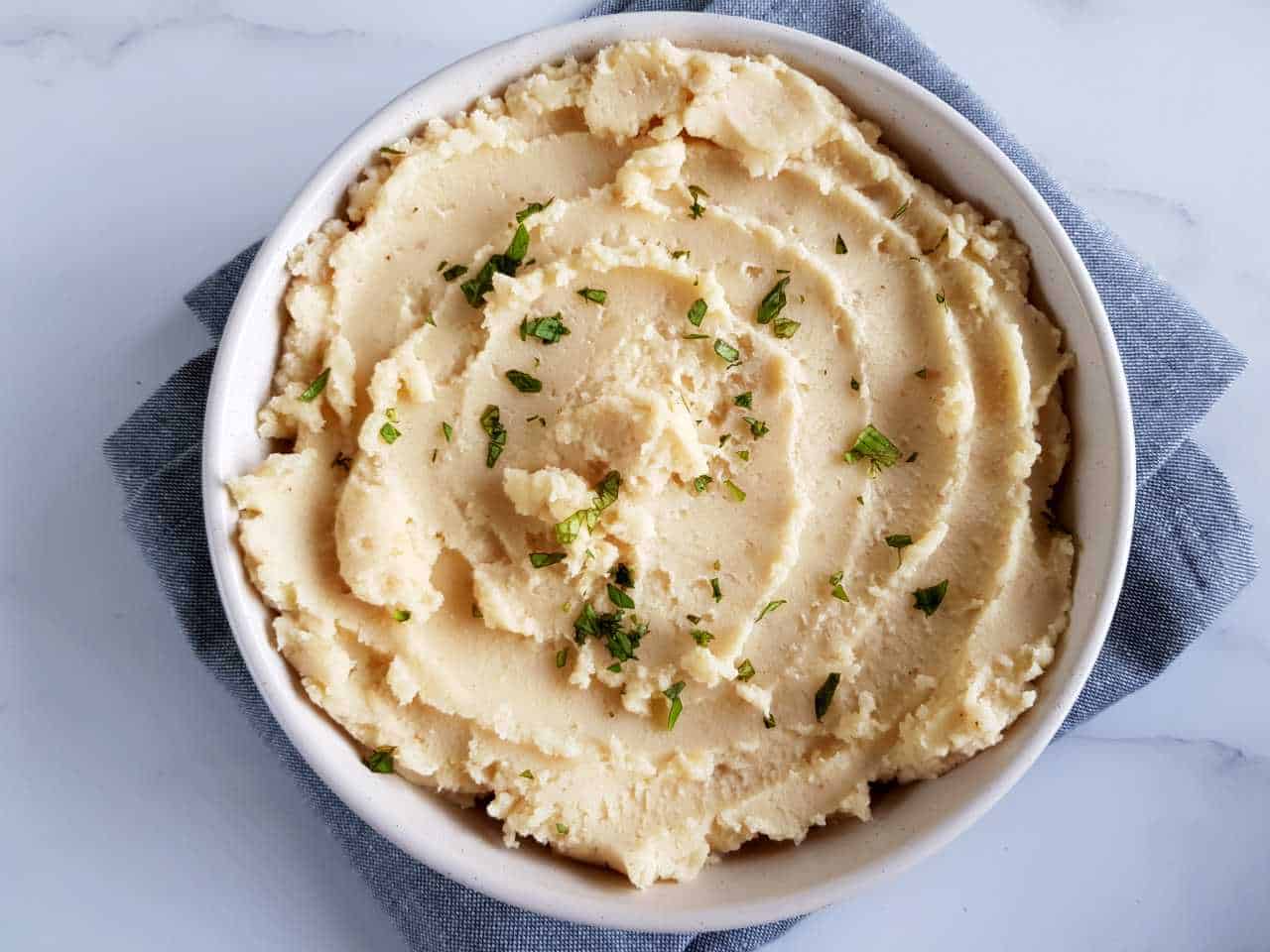 Creamy mashed potatoes in a white bowl on a marble table