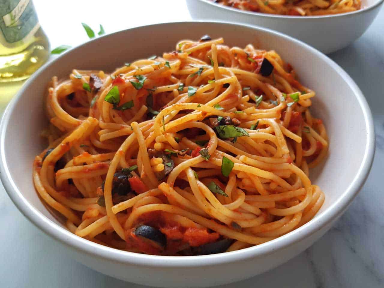 Spaghetti alla puttanesca in a white bowl on a marble table.