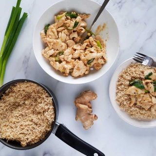 Spring onion and ginger chicken in a bowl with a pot of rice on the side.