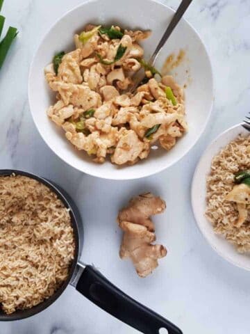 Spring onion and ginger chicken in a bowl with a pot of rice on the side.