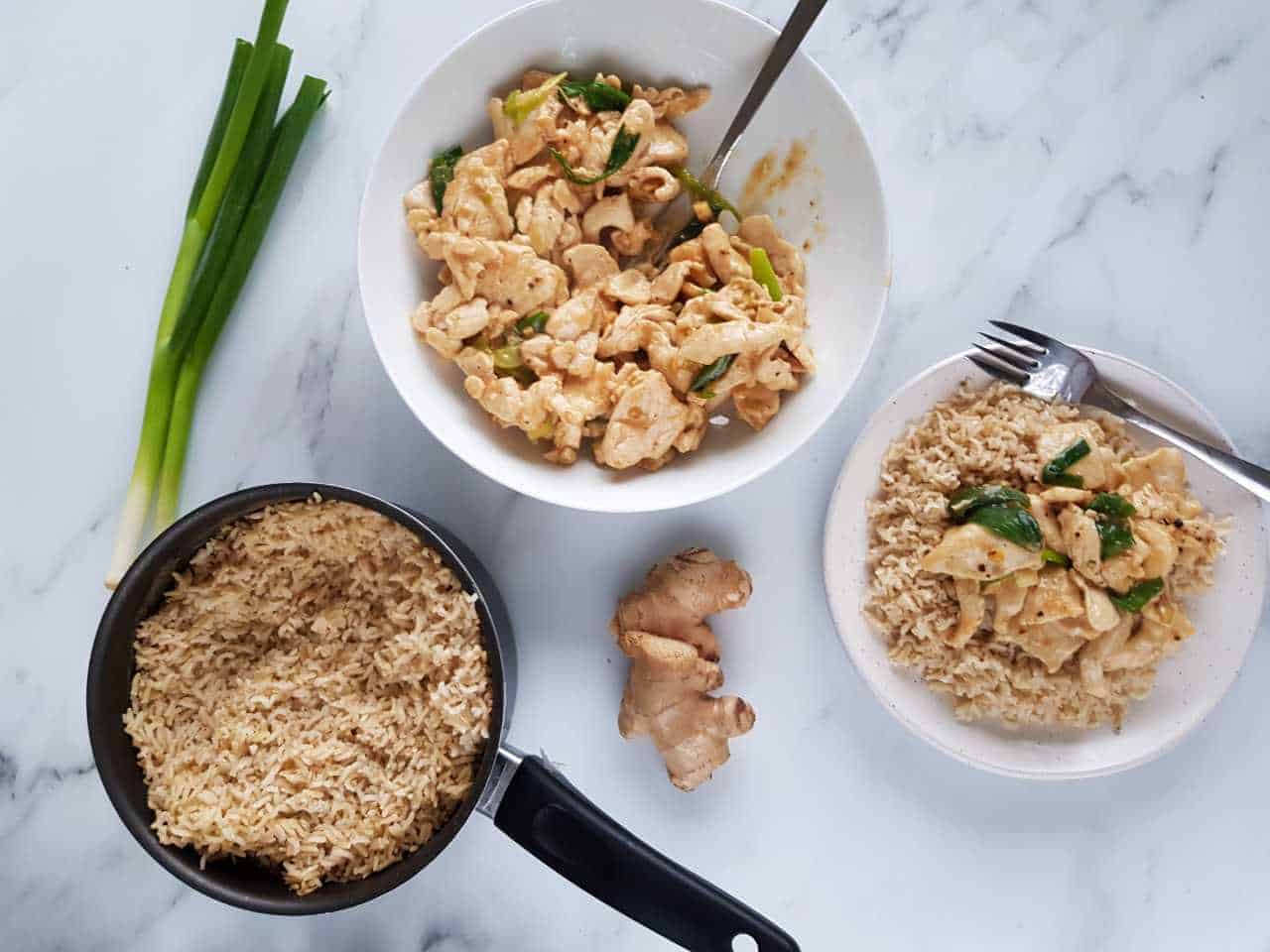 Spring onion and ginger chicken in a bowl with a pot of rice on the side.