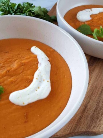 Thai curried sweet potato soup in white bowls on a wooden board.