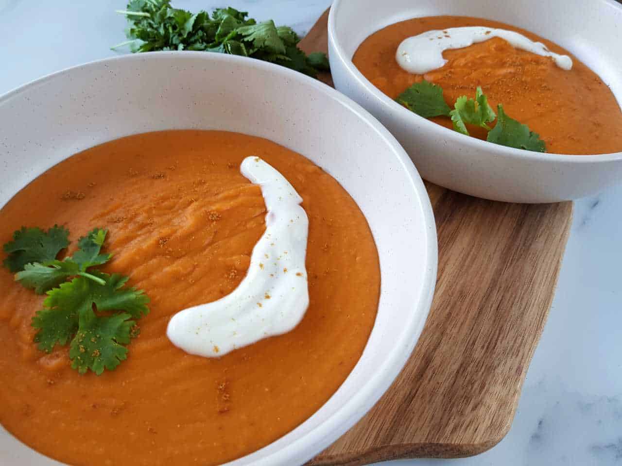 Thai curried sweet potato soup in white bowls on a wooden board.