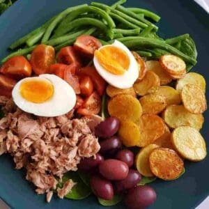 a plate of nicoise salad with eggs, tuna,potatoes and green beans.