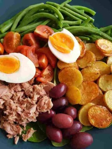 a plate of nicoise salad with eggs, tuna,potatoes and green beans.