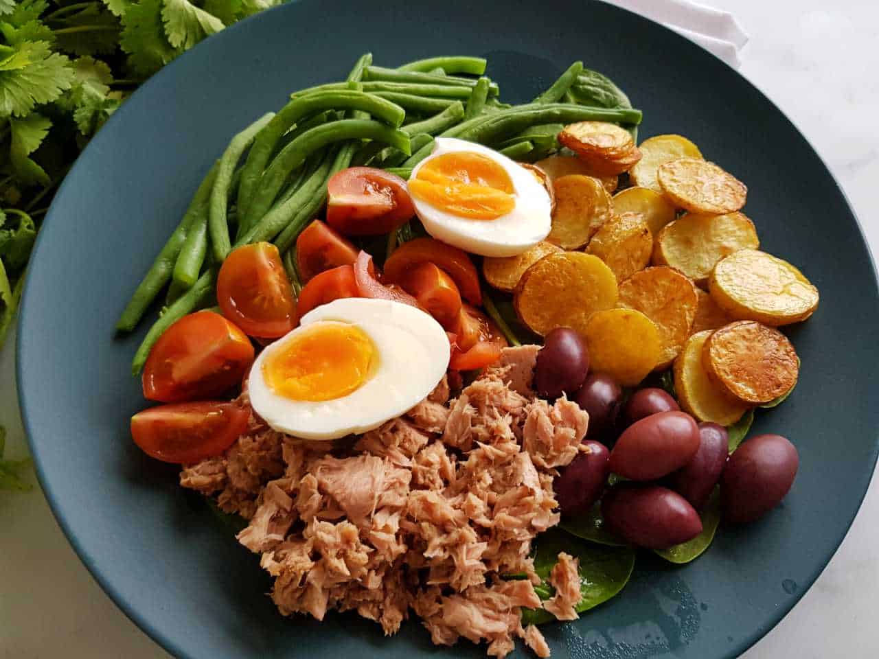 Tuna nicoise salad on a blue plate on a marble table.