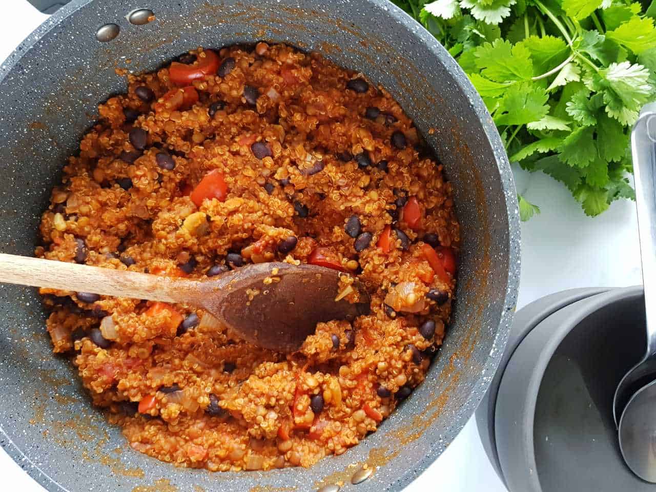 Vegetarian chili with quinoa in a large pot with gray bowls an dfresh coriander on the side.