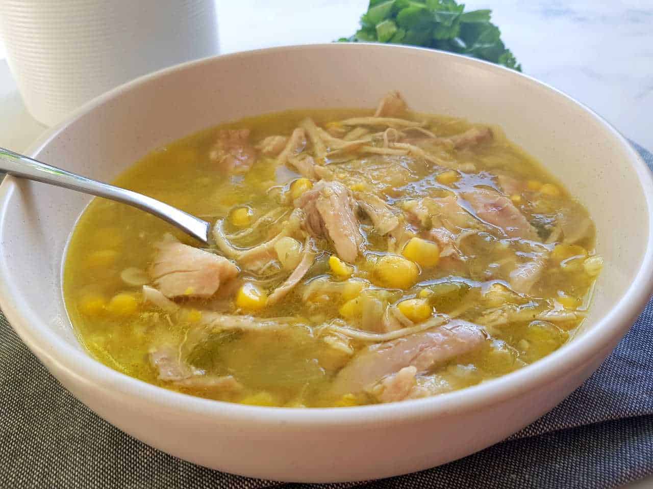 chicken & sweetcorn soup in a white bowl with herbs in the background.