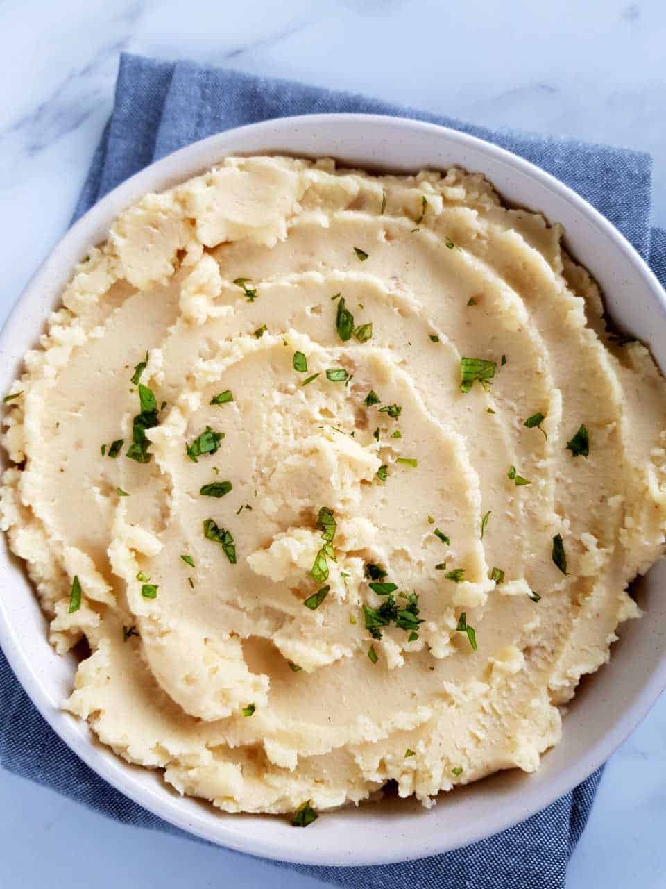 Mashed potatoes in a white bowl topped with fresh herbs.