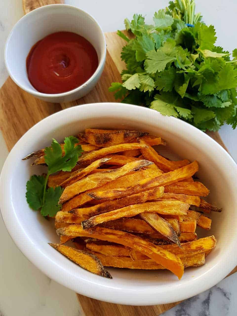 sweet potato fries on a wooden board with tomato sauce and fresh herbs.