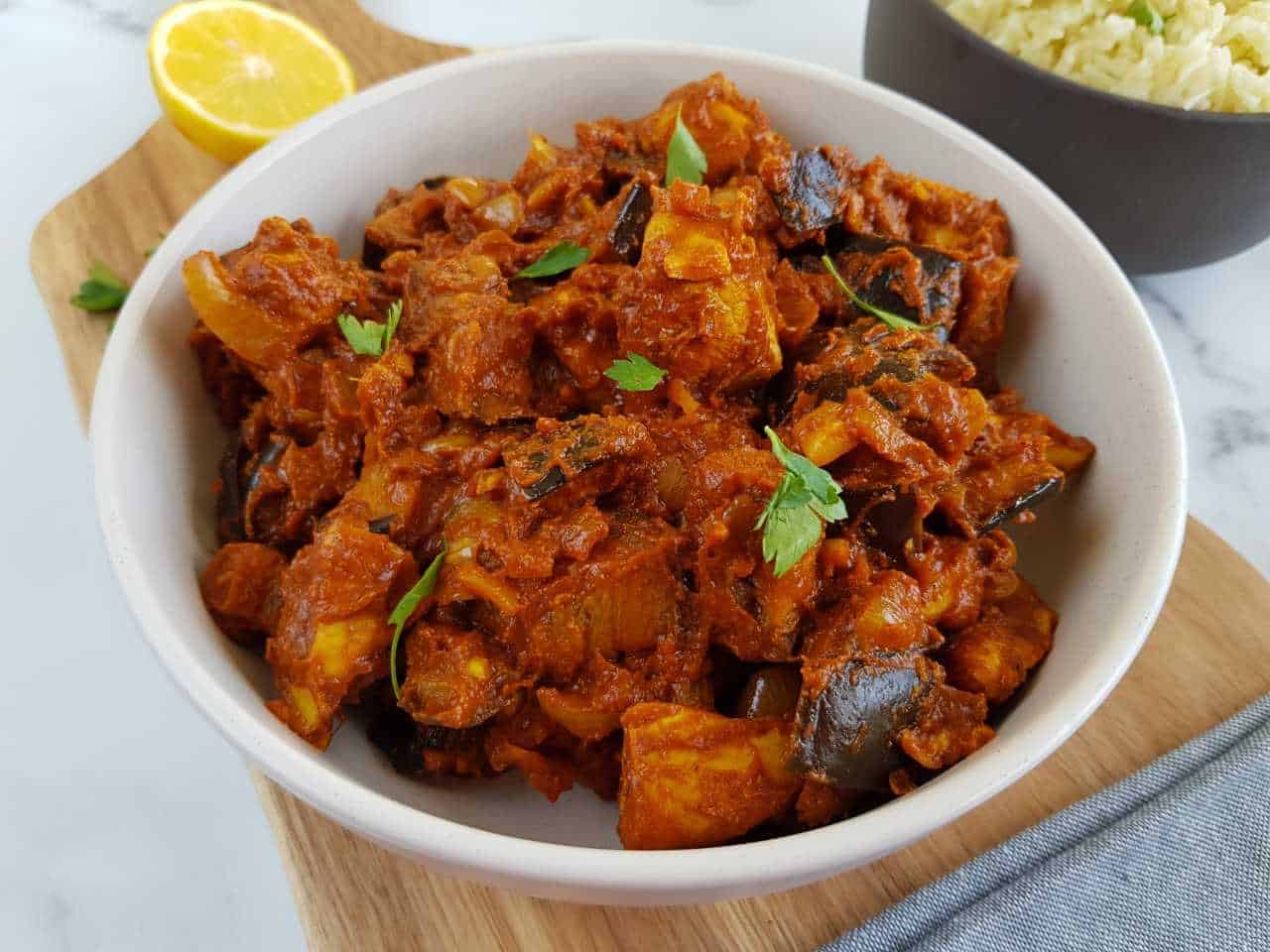 Chicken and aubergine curry in a white bowl.