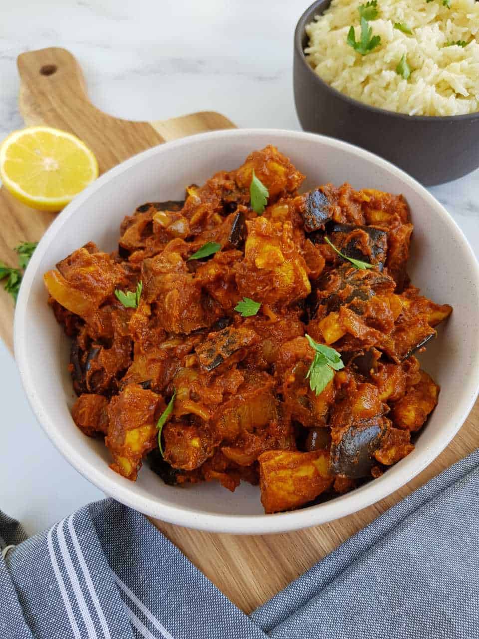 Chicken and aubergine curry in a bowl with rice and fresh lemon in the background.