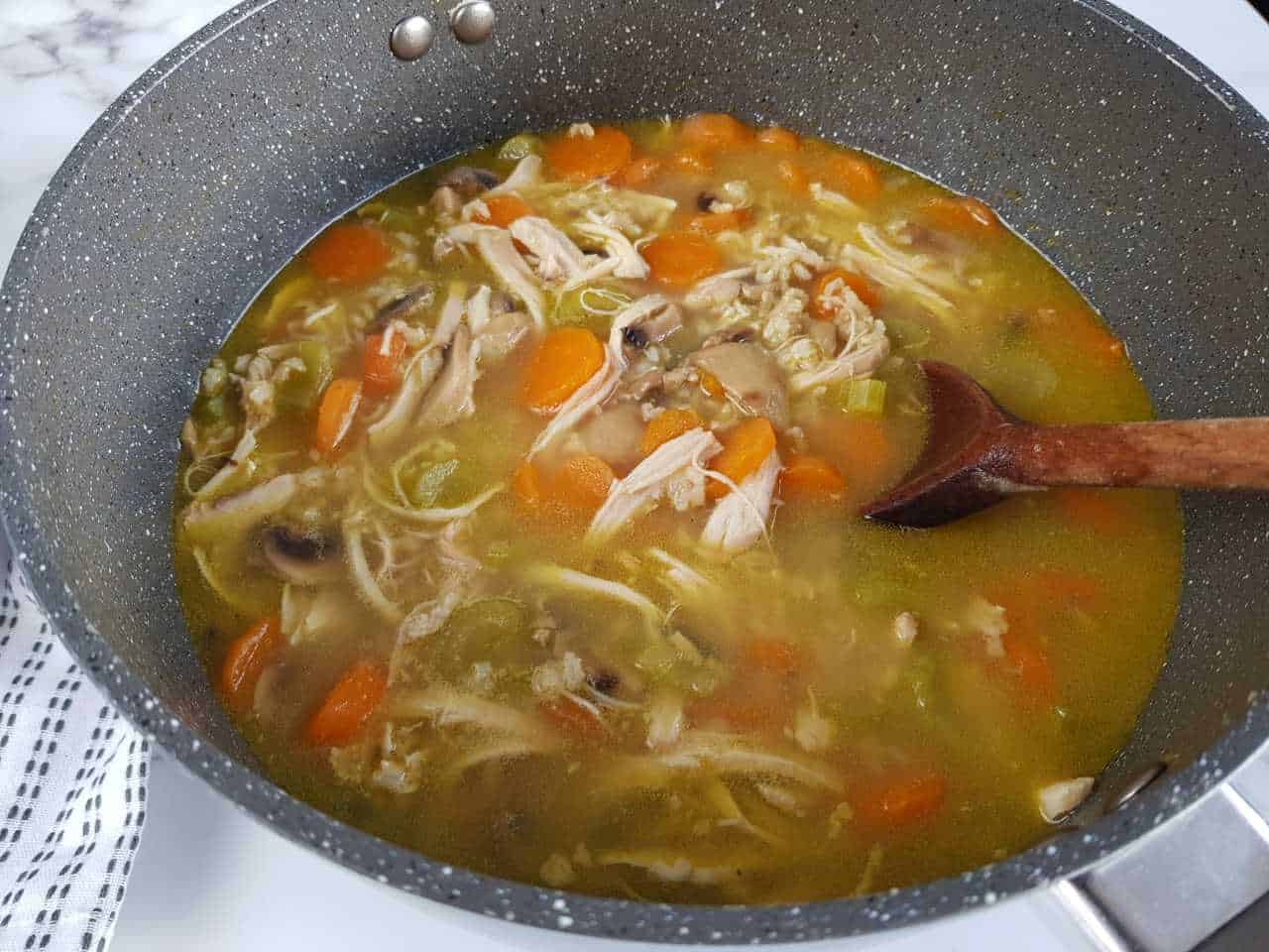 Chicken and rice soup in a gray pot with a wooden spoon.