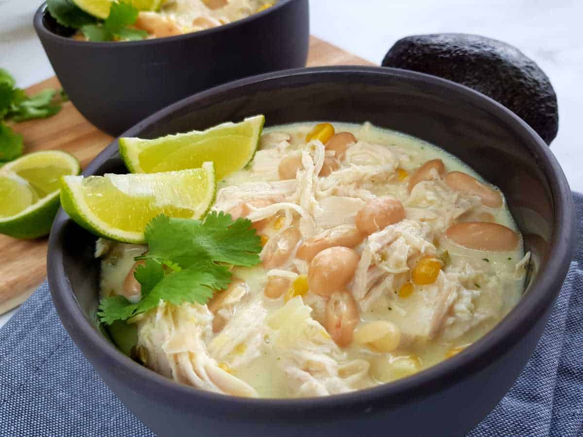 White chicken chili in gray bowls with lime and herbs on top.