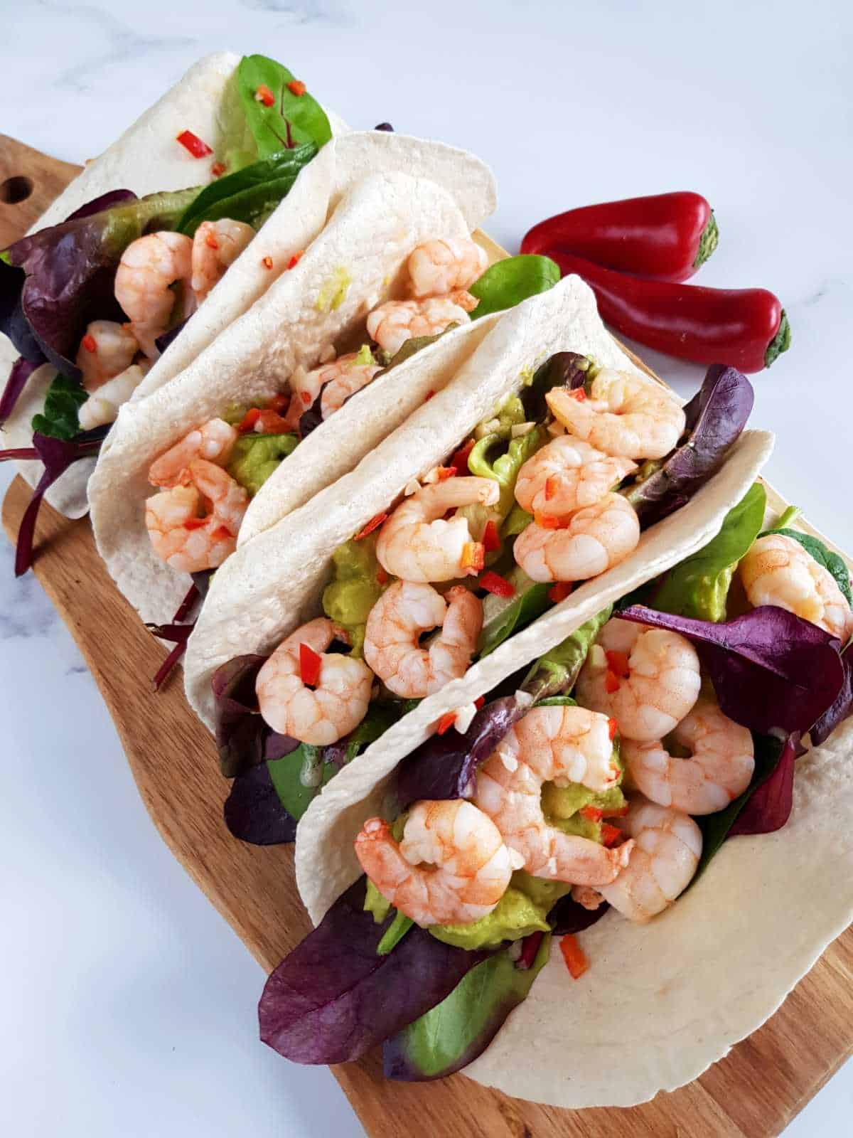 Chili and lime shrimp tacos on a wooden board.