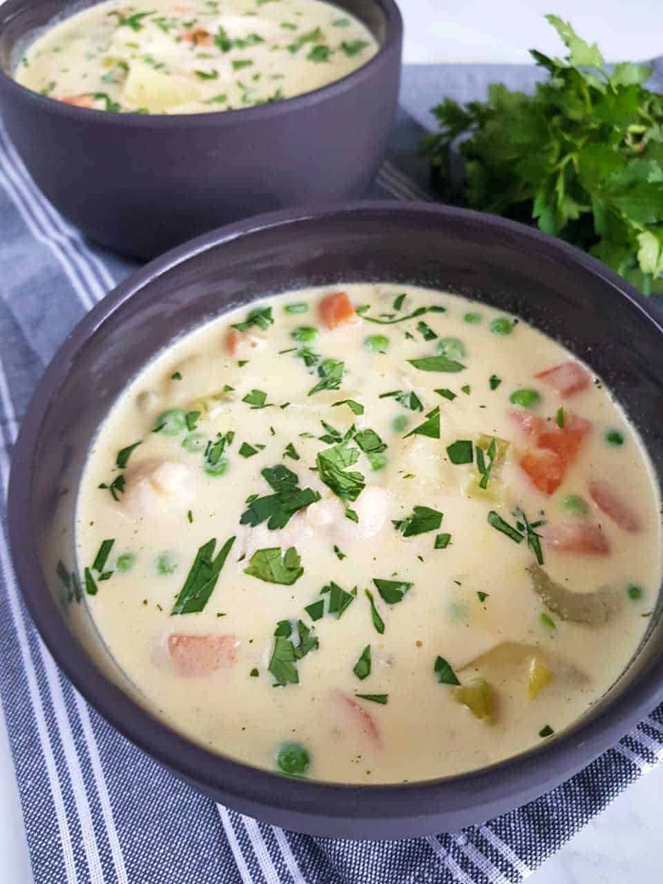 creamy chicken and vegetable soup in gray bowls on a gray table cloth.