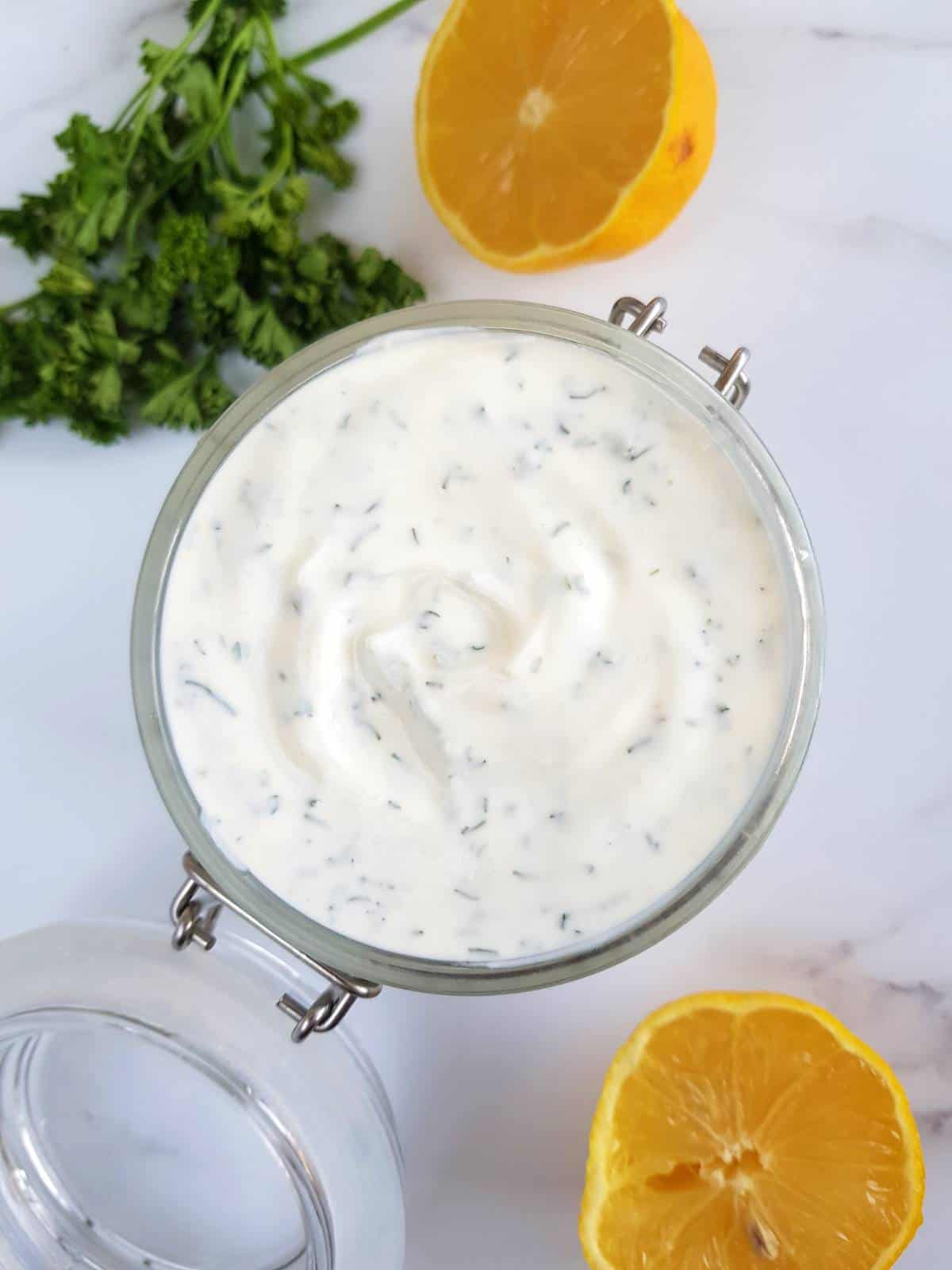 Creamy homemade ranch in a jar with lemon and parsley on the side.