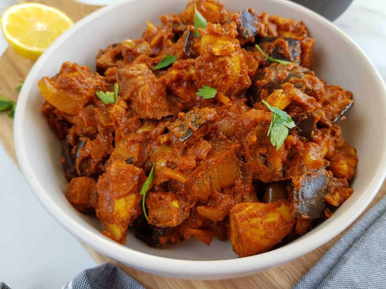 Chicken and aubergine curry in a white bowl with lemon in the background.