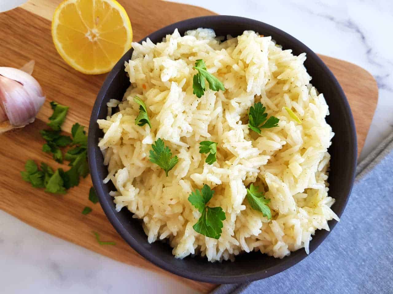 Lemon garlic rice in a black bowl with lemon and garlic in the background.