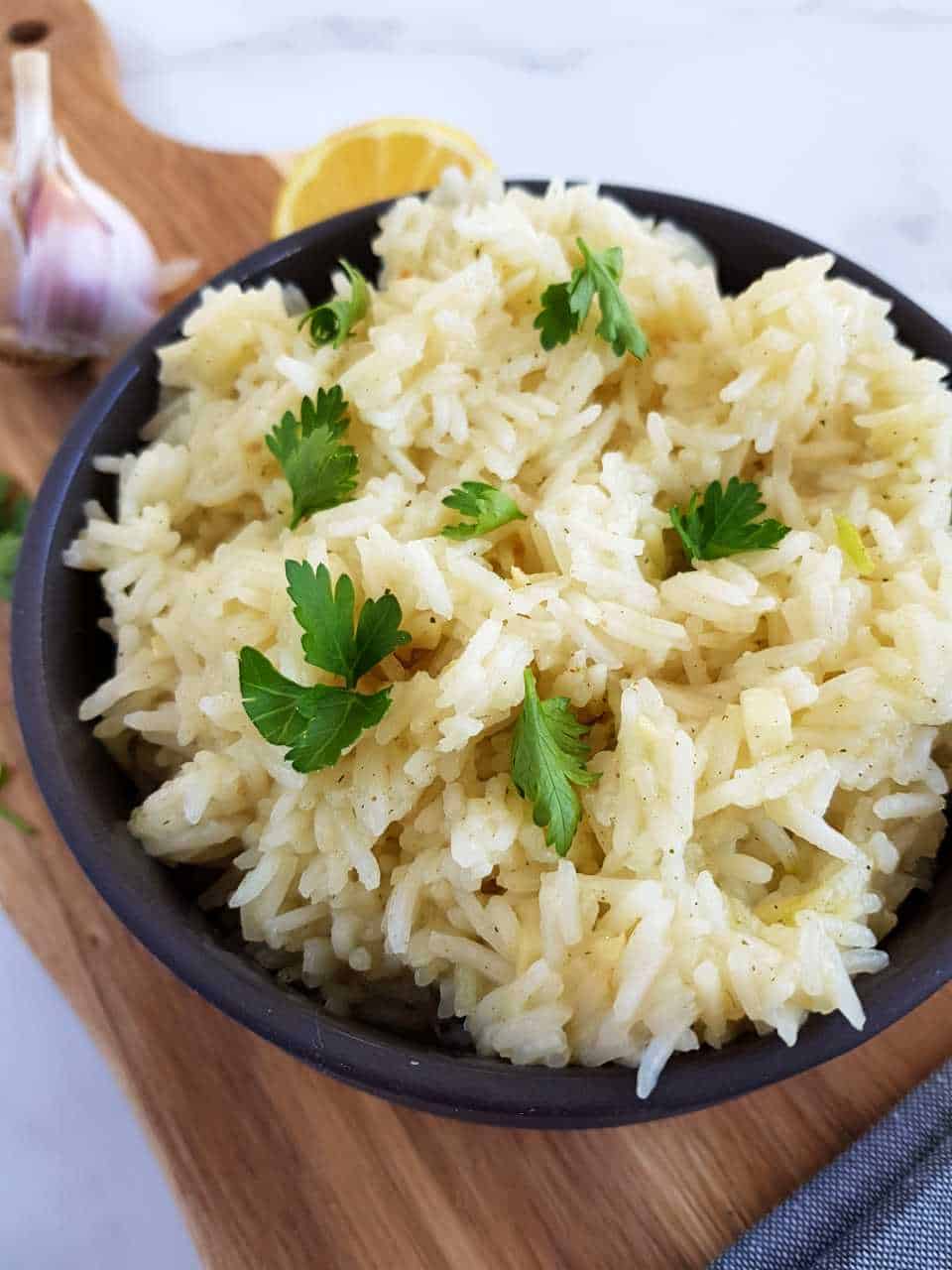 Lemon garlic rice in a black bowl with lemon and garlic in the background.