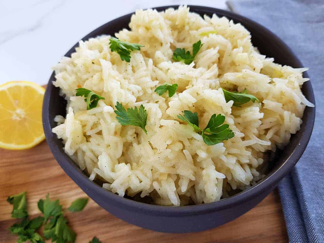 Lemon garlic rice in a black bowl with lemon and fresh herbs in the background.