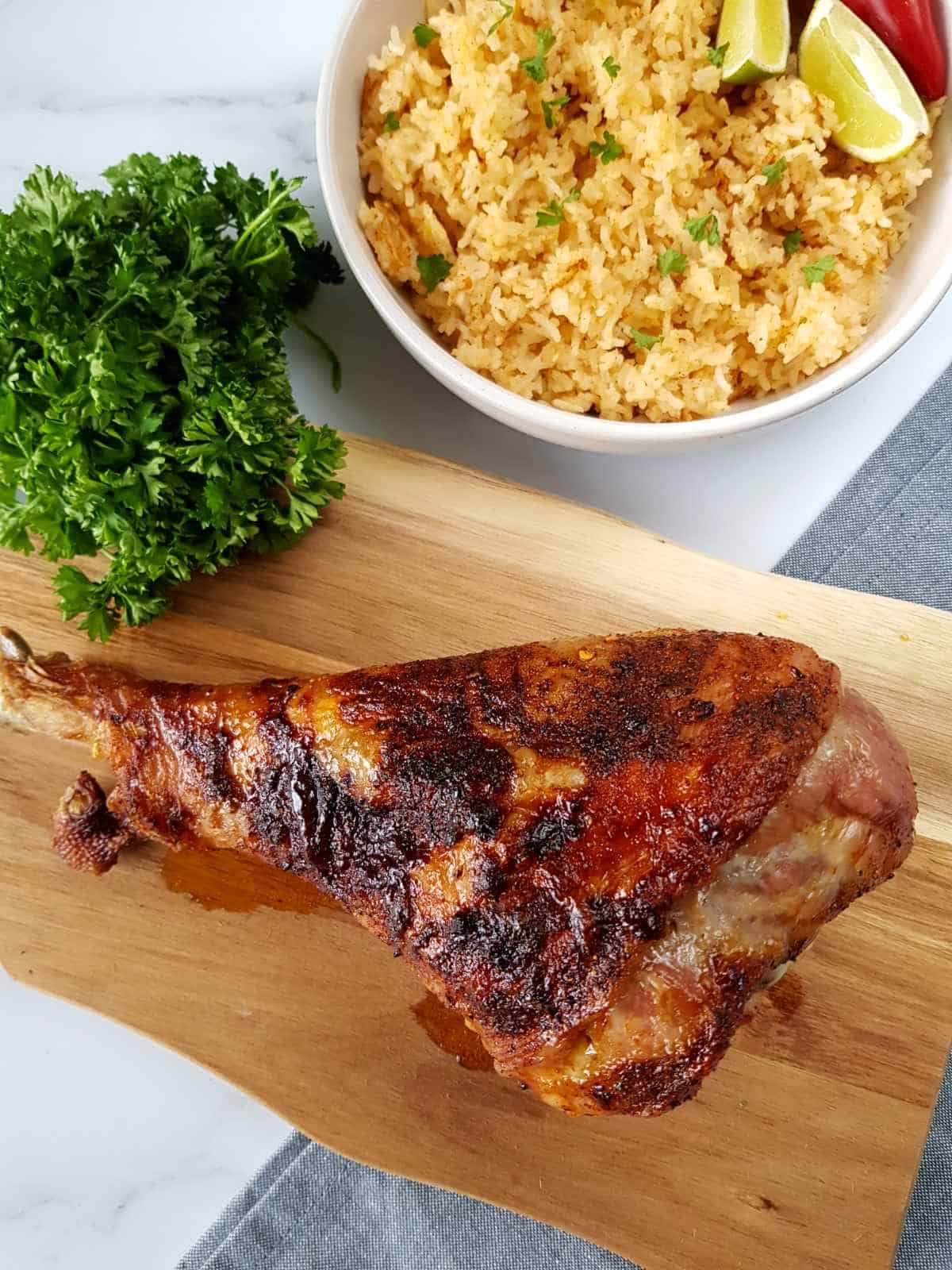 Moroccan roasted turkey drumstick on a wooden board with fresh herbs and rice on the side.