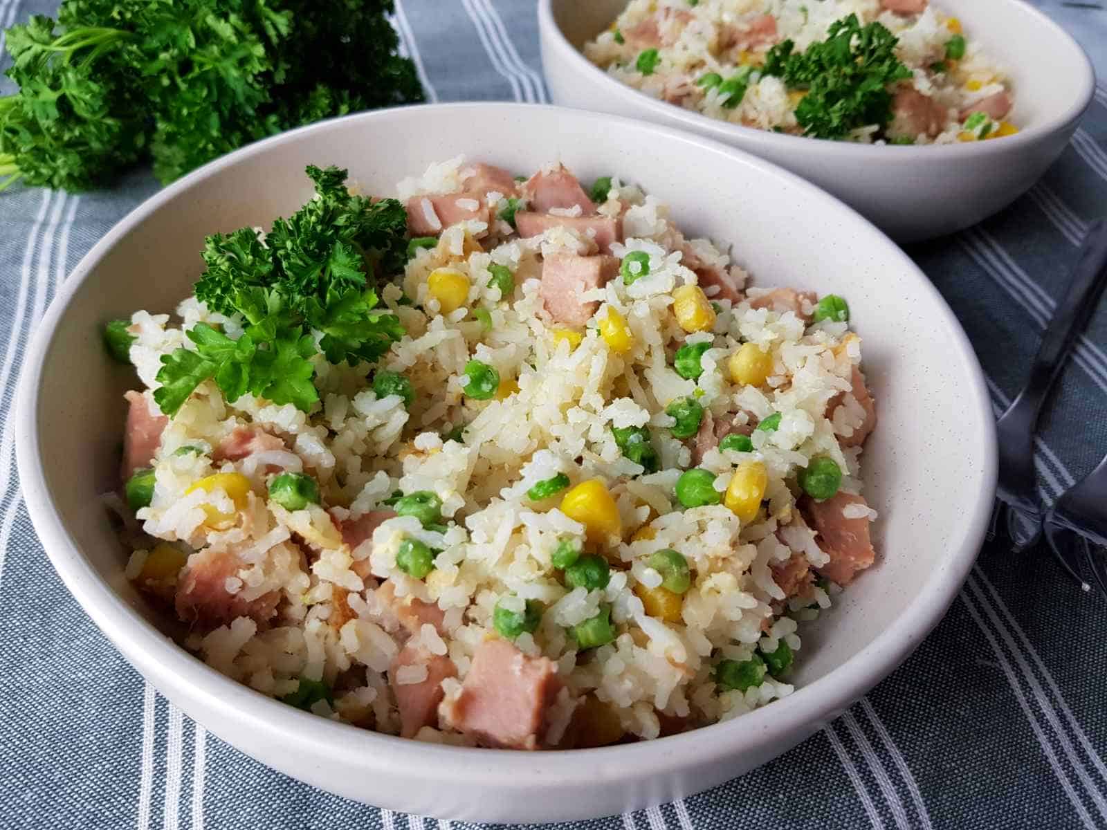 Gammon fried rice in white bowls on a tablecloth with fresh herbs.