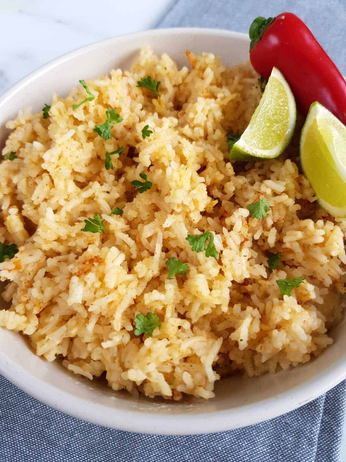 Rice with chili and lime in a white bowl, garnished with lime wedges and fresh chili.