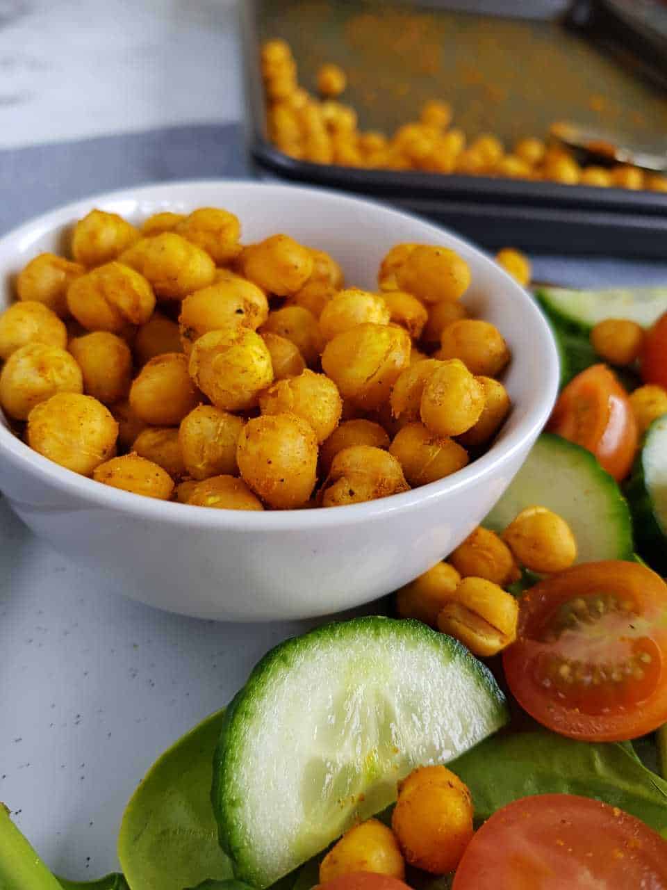 Roasted chickpeas with turmeric in a white bowl with salad on the side.