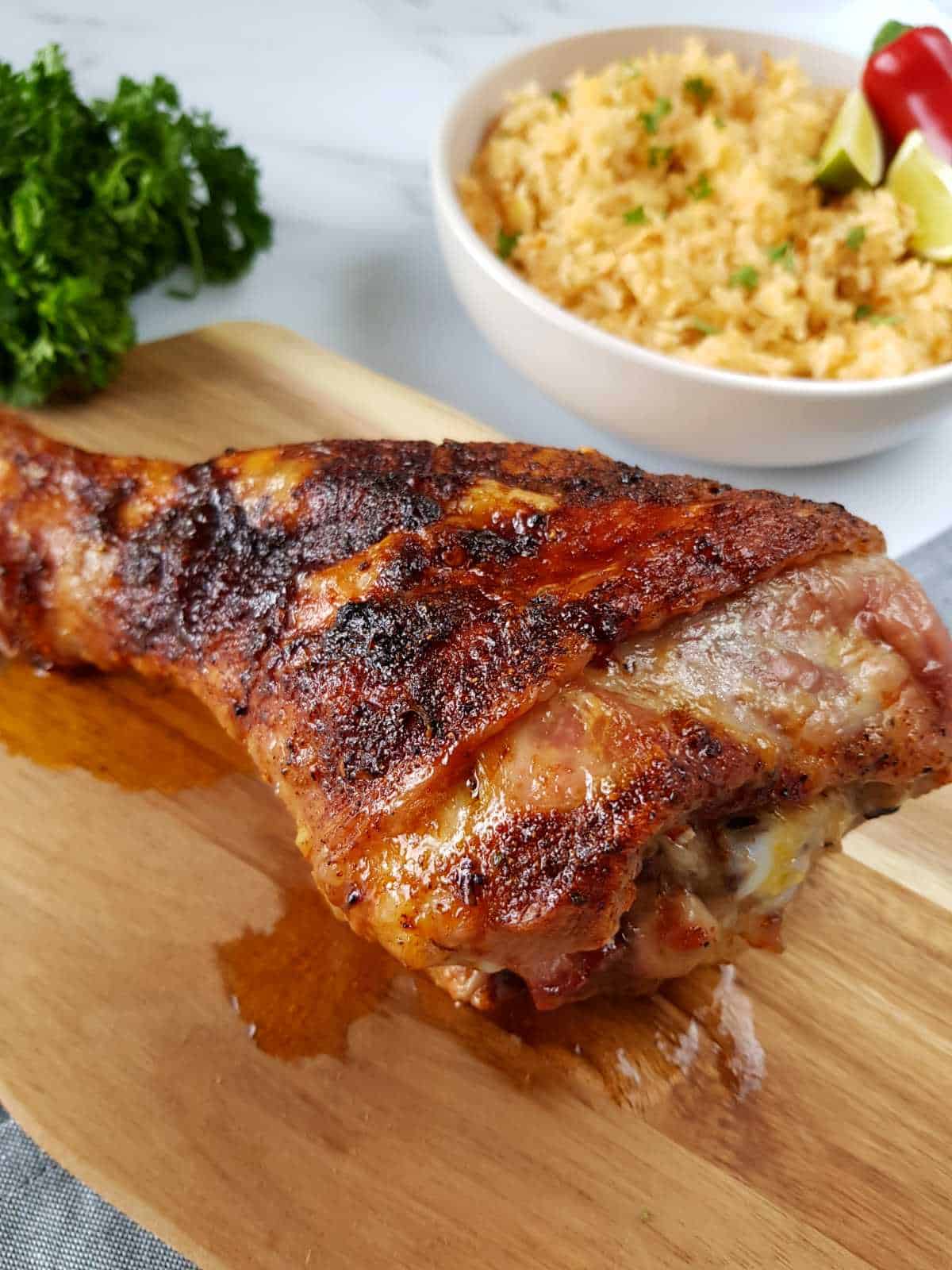 Roasted turkey drumstick Moroccan style on a wooden board with rice and herbs in the background.