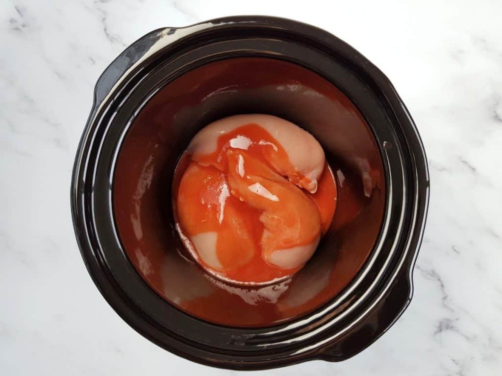 Chicken breast fillets with buffalo sauce in a slow cooker.