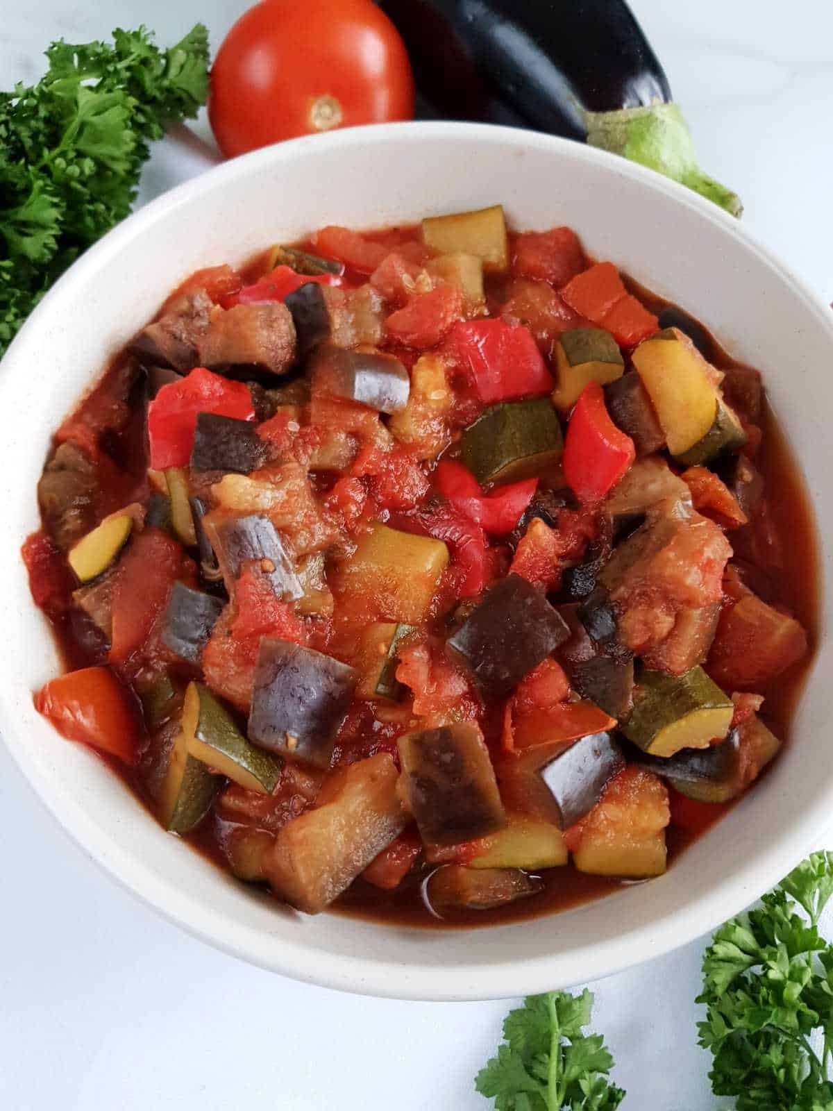 Slow cooker ratatouille in a white bowl with fresh vegetables in the background.