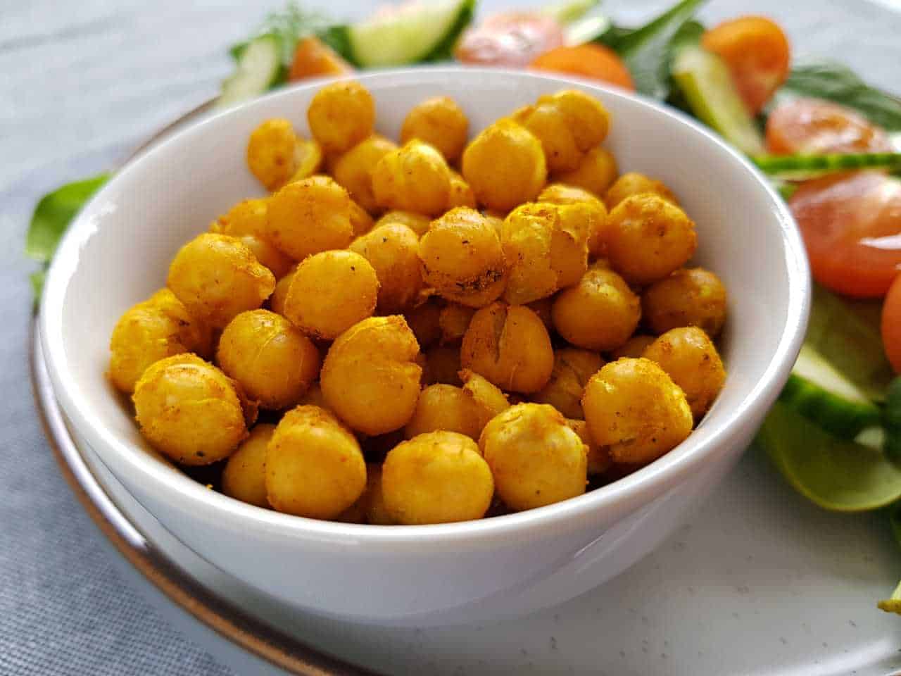 Turmeric roasted chickpeas in a white bowl with salad in the background.