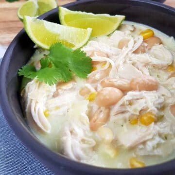 White chicken chili in gray bowls with lime and herbs on top