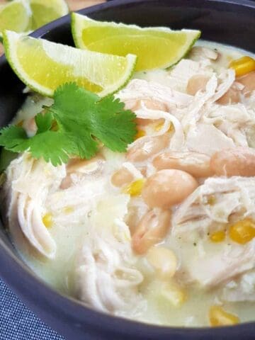 White chicken chili in gray bowls with lime and herbs on top