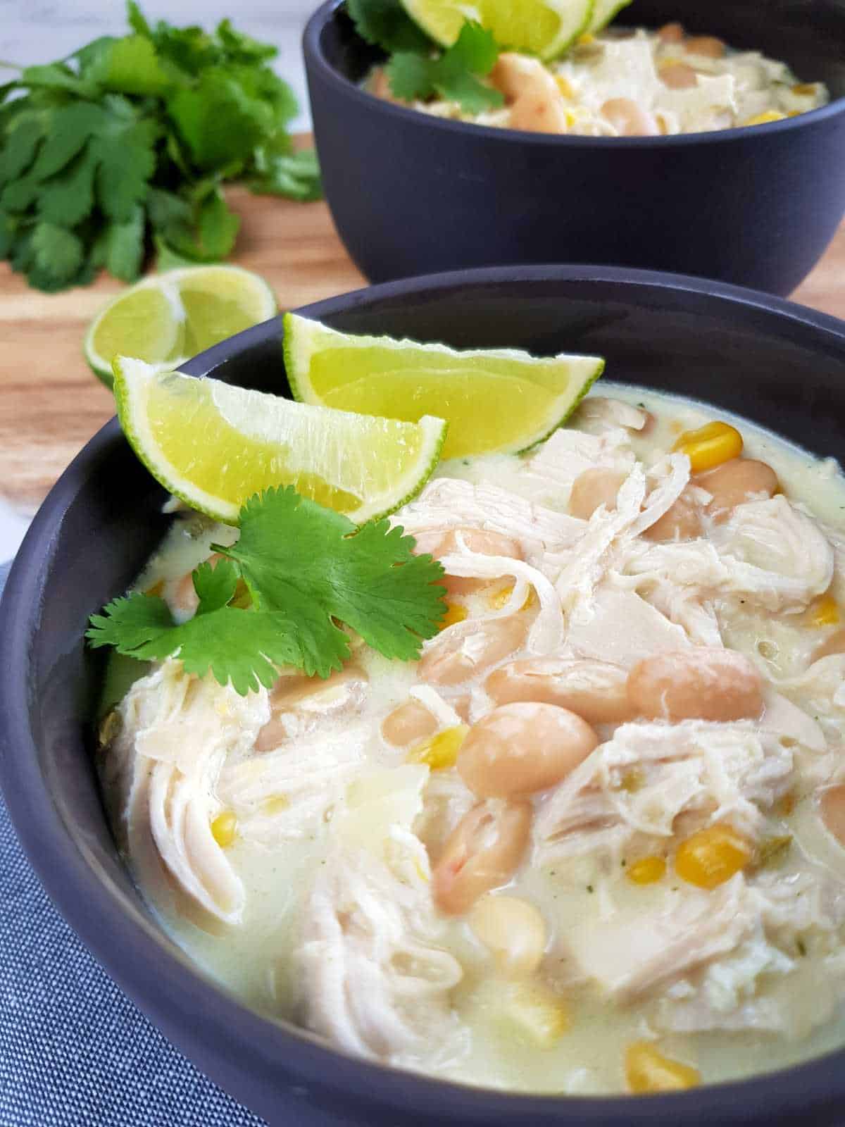 White chicken chili in gray bowls with lime and herbs on top,